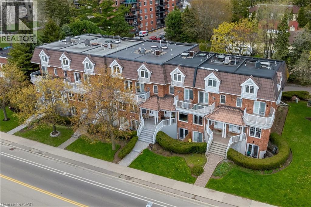Brick facade property featuring multiple balconies with white railings, dormer windows, a brown mansard-style roof, and landscaped grounds - 1389 Lakeshore Road, Burlington, ON - Outdoor With Facade