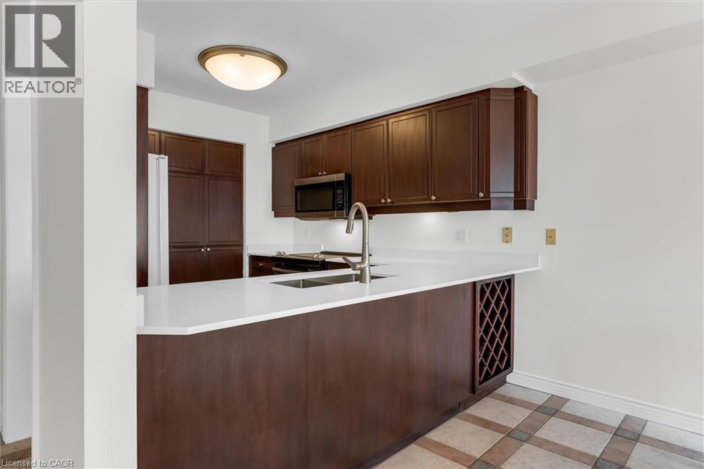 Kitchen featuring dark wood cabinetry, light countertops, built-in wine rack, and tile flooring - 1389 Lakeshore Road, Burlington, ON - Indoor Photo Showing Kitchen With Double Sink