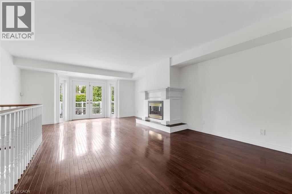 Spacious room featuring rich wood-finish flooring, a contemporary fireplace with a classic mantel, and double French doors opening to a balcony - 1389 Lakeshore Road, Burlington, ON - Indoor With Fireplace