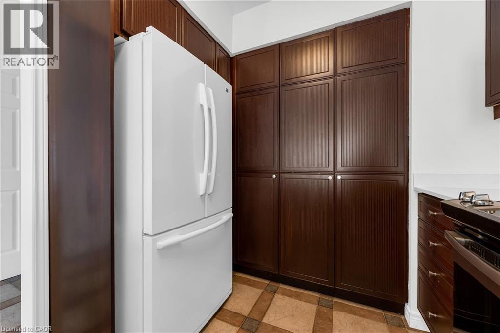 Kitchen featuring extensive dark wood-finish cabinetry, an integrated white refrigerator, white countertops, and patterned floor tiling - 1389 Lakeshore Road, Burlington, ON - Indoor