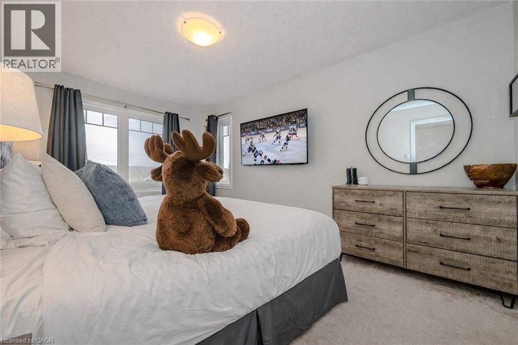 Bright bedroom featuring a large window with multiple panes, a flush-mount ceiling light, and light-toned carpeting - 525 Cavanagh Lane, Milton, ON - Indoor Photo Showing Bedroom
