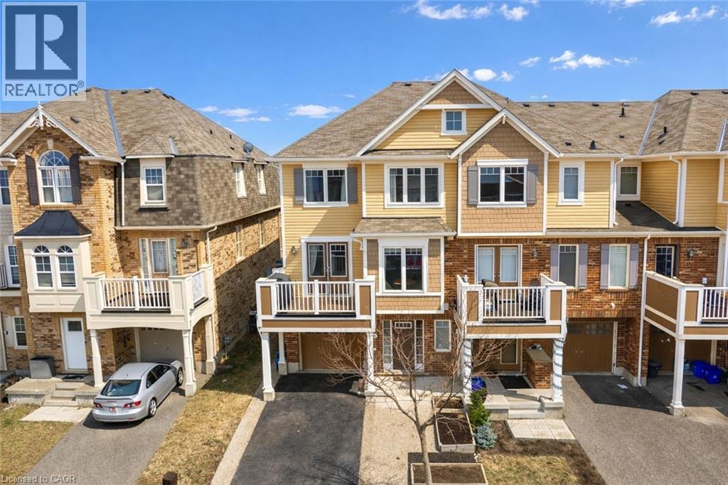 Multi-level townhouse featuring a two-tone facade with brick and siding, multiple balconies with white railings, and an integrated single-car garage - 525 Cavanagh Lane, Milton, ON - Outdoor With Facade