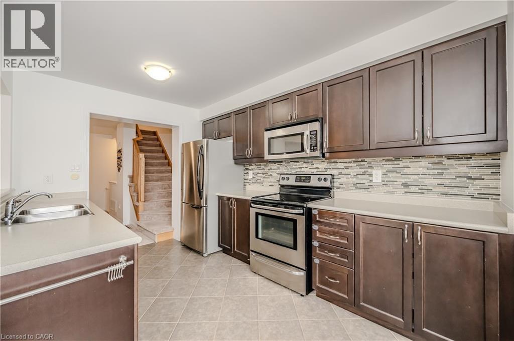 Kitchen featuring dark wood-finish cabinetry, stainless steel appliances, light-toned countertops, and a mosaic tile backsplash - 525 Cavanagh Lane, Milton, ON - Indoor Photo Showing Kitchen With Double Sink