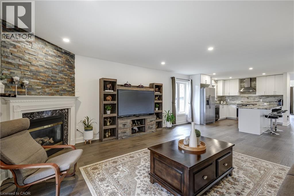 Spacious living area featuring a stone accent wall, fireplace with white mantel, and wood-finish flooring - 29 Wiltshire Place, Ancaster, ON - Indoor Photo Showing Living Room With Fireplace