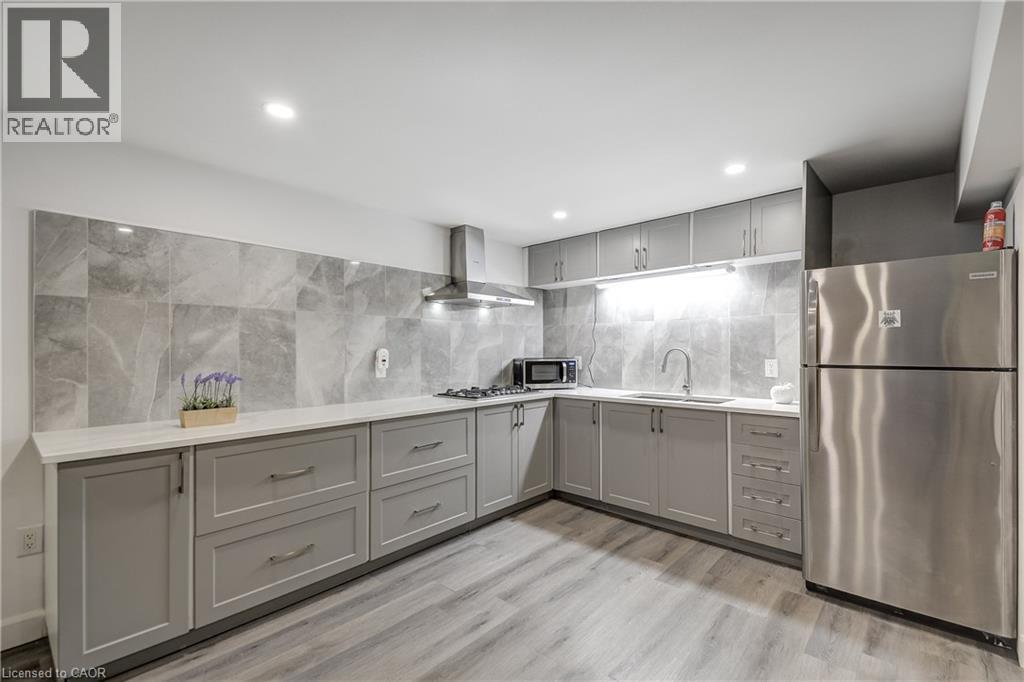 Contemporary kitchen featuring L-shaped gray cabinetry, stainless steel appliances, light-toned countertops, and a gray tile backsplash - 29 Wiltshire Place, Ancaster, ON - Indoor Photo Showing Kitchen With Upgraded Kitchen