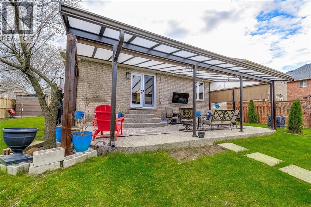 Expansive covered patio featuring a concrete surface, direct access via double doors, a brick exterior, and a manicured lawn with stepping stones - 29 Wiltshire Place, Ancaster, ON - Outdoor