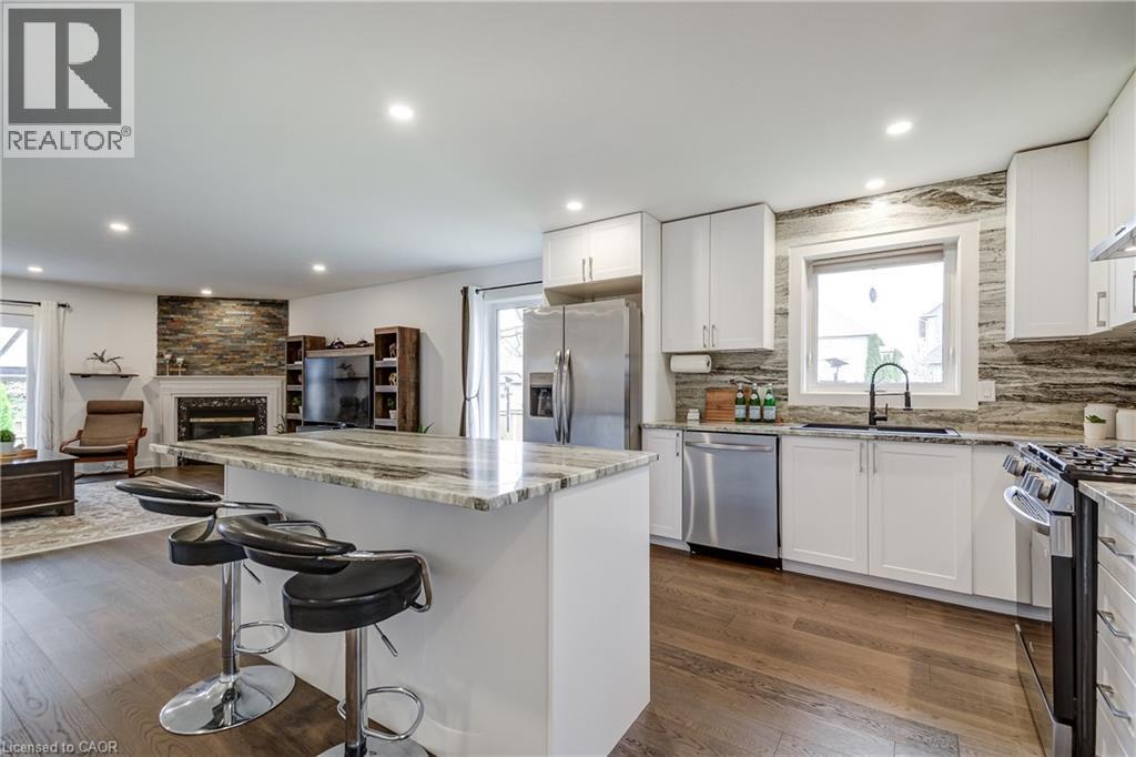 Open-concept kitchen featuring an island with a stone countertop, white cabinetry, stainless steel appliances, and wood-finish flooring - 29 Wiltshire Place, Ancaster, ON - Indoor Photo Showing Kitchen With Upgraded Kitchen