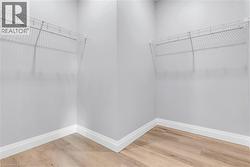 Walk-in closet with light gray walls, white wire shelving, white baseboards, and wood-finish flooring -