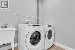 Dedicated laundry area featuring a utility sink, a front-loading washer and dryer, light gray wall paint, white baseboards, and a wall-mounted wire shelf -