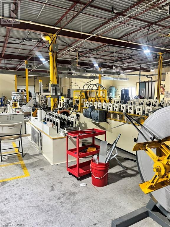 Industrial space featuring high ceilings with exposed structural beams, fluorescent lighting, concrete flooring with yellow safety markings, and large-scale manufacturing equipment - 550 Parkside Drive Unit# A13-16, Waterloo, ON