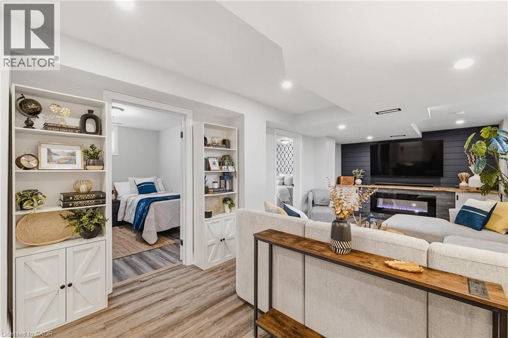 Open concept living space featuring wood-finish flooring, a built-in electric fireplace with a stone surround, and an accent wall with shiplap paneling - 120 Elgin Crescent, Waterloo, ON - Indoor With Fireplace