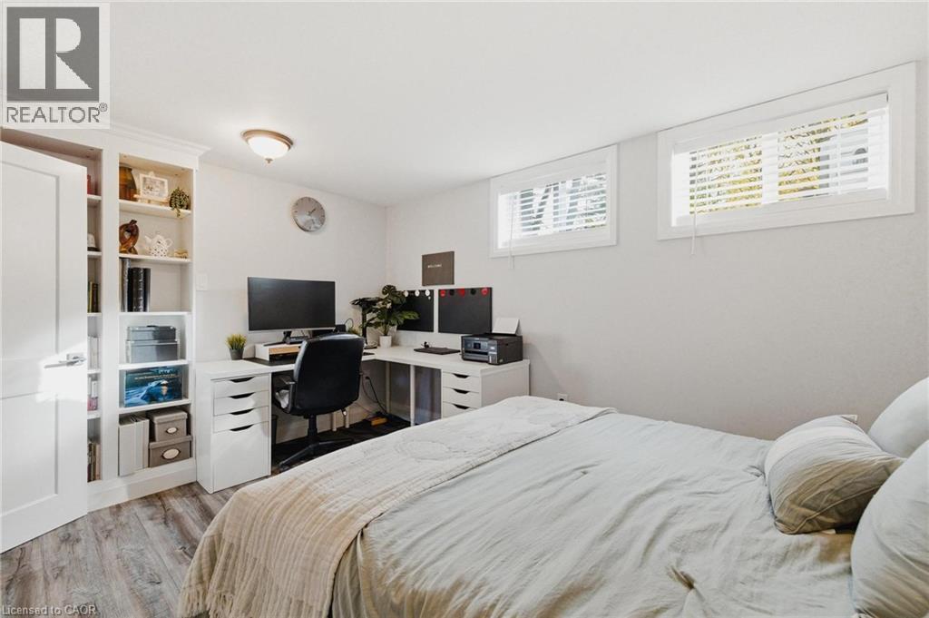 Bedroom featuring wood-finish flooring, built-in shelving, two transom windows with white blinds, and a white interior door - 120 Elgin Crescent, Waterloo, ON - Indoor Photo Showing Bedroom