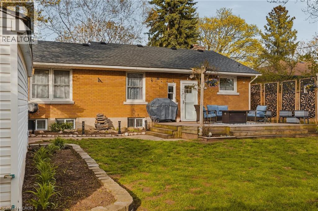 Expansive backyard featuring a raised wood-finish deck with privacy screens, a brick exterior with white trim windows, a manicured lawn, and defined garden beds - 120 Elgin Crescent, Waterloo, ON - Outdoor