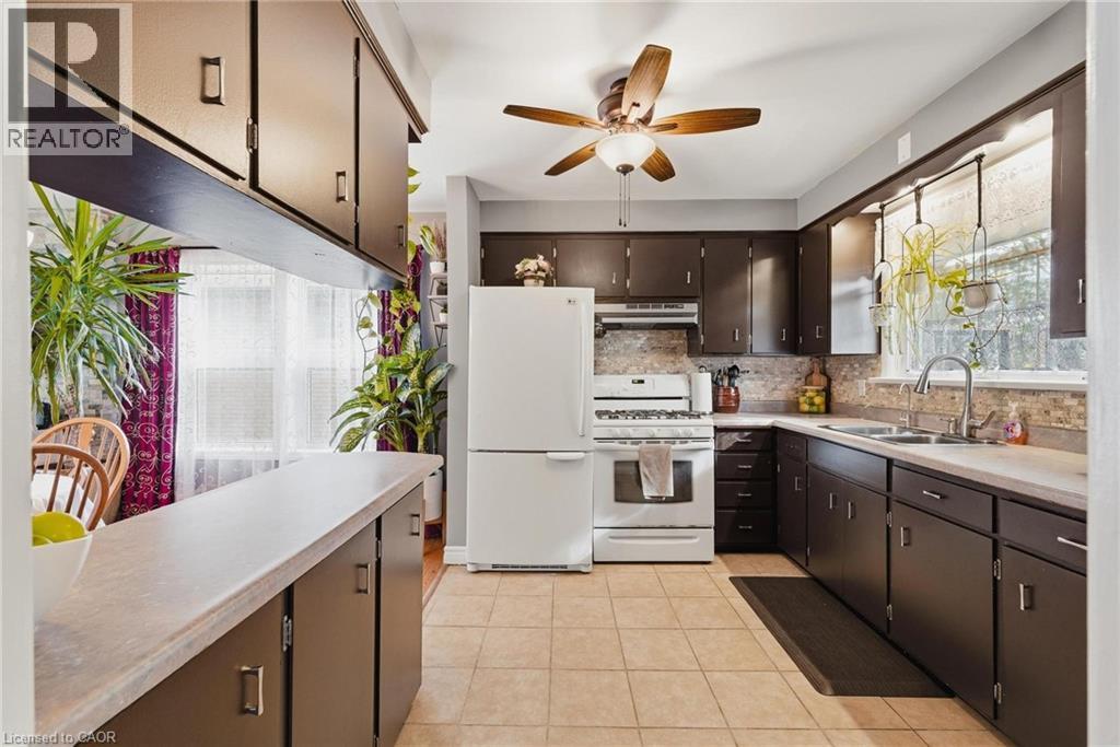Kitchen featuring dark wood cabinetry, light-toned countertops, white appliances, and tan tiled flooring - 120 Elgin Crescent, Waterloo, ON - Indoor Photo Showing Kitchen With Double Sink