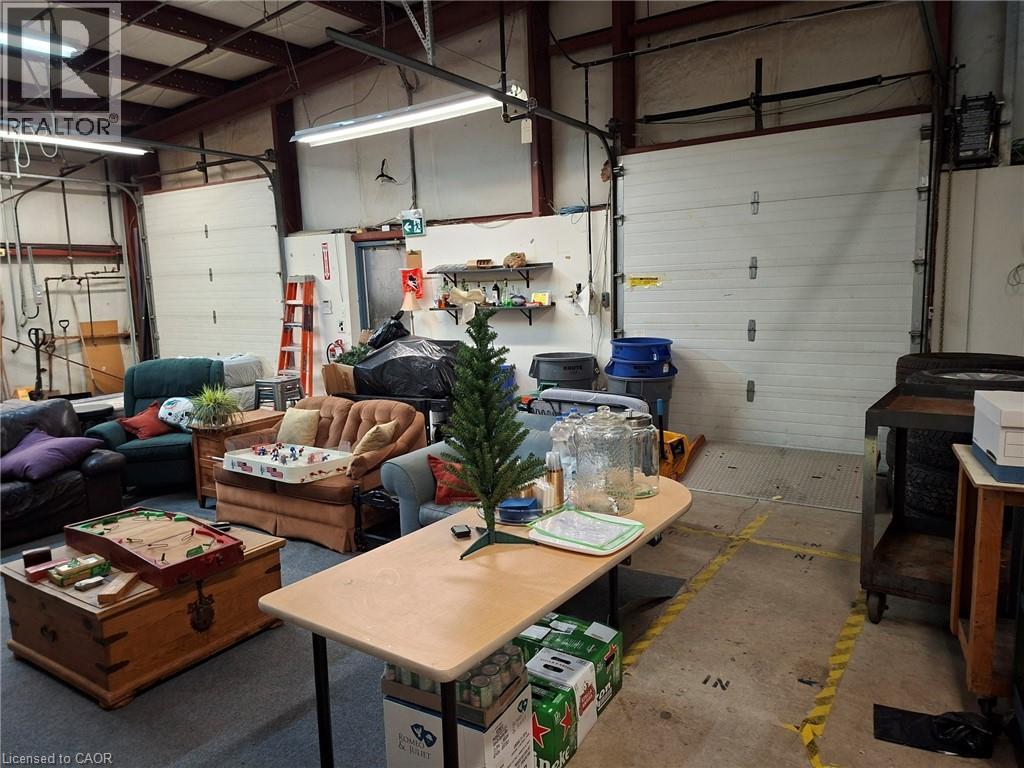 Warehouse space featuring exposed beam ceilings, industrial fluorescent lighting, two white panel roll-up doors, and concrete flooring with yellow safety striping - 920 Sheldon Court, Burlington, ON