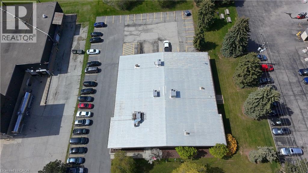 Aerial perspective of a commercial property featuring a large building with a light-colored roof, multiple parking areas, and mature landscaping - 920 Sheldon Court, Burlington, ON