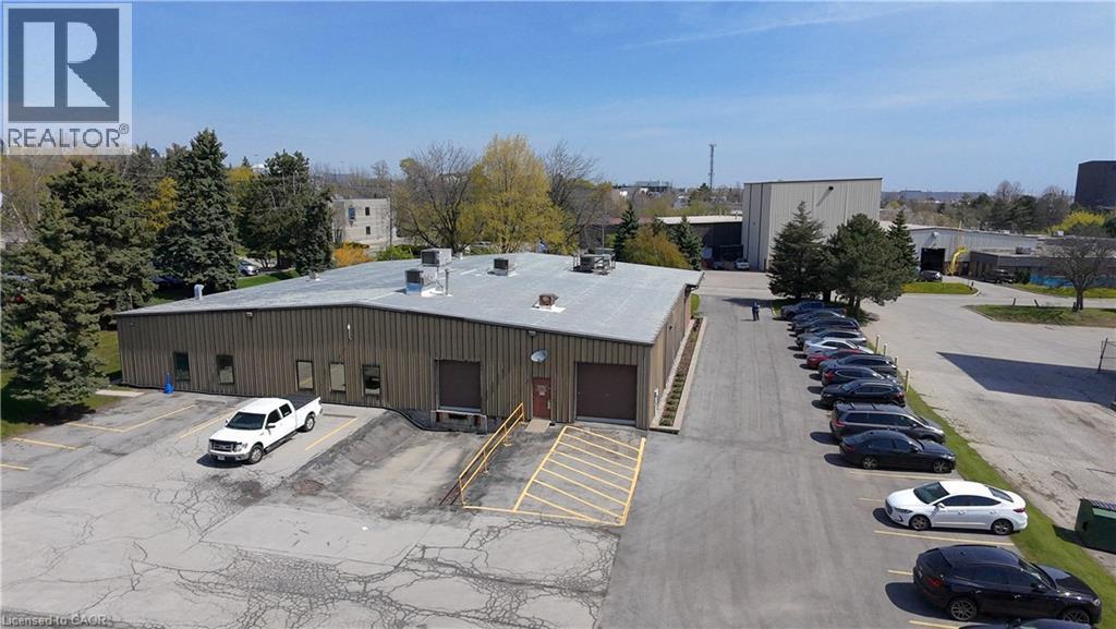 Commercial building featuring corrugated metal siding, multiple loading dock doors, a dedicated parking lot, and surrounding mature trees - 920 Sheldon Court, Burlington, ON