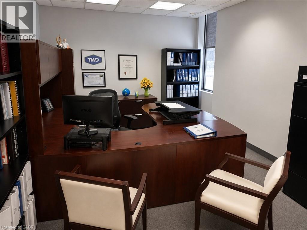 Spacious office featuring a wood-finish desk with an integrated hutch, built-in shelving, a large window with a roller shade, and ceiling-mounted fluorescent lighting - 920 Sheldon Court, Burlington, ON