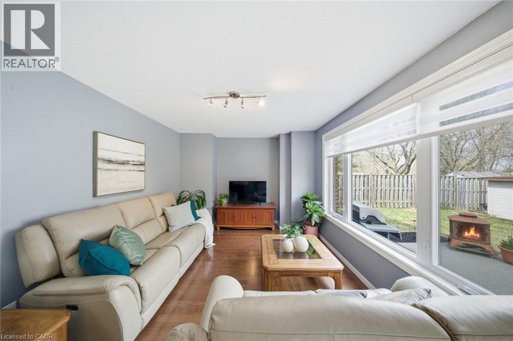 Living area featuring large windows with white blinds, wood-finish flooring, light blue walls, and a track light fixture - 200 Morrison Drive, Caledonia, ON - Indoor Photo Showing Living Room