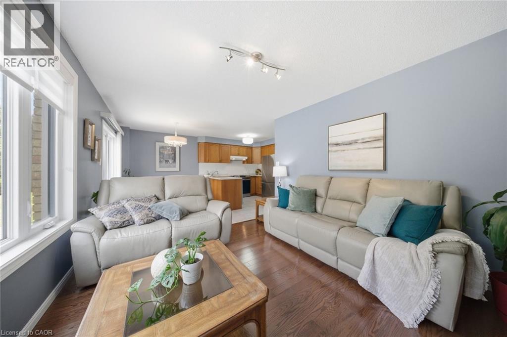 Open-concept living area with wood-finish flooring, abundant natural light from multiple windows, and a recessed kitchen beyond - 200 Morrison Drive, Caledonia, ON - Indoor Photo Showing Living Room
