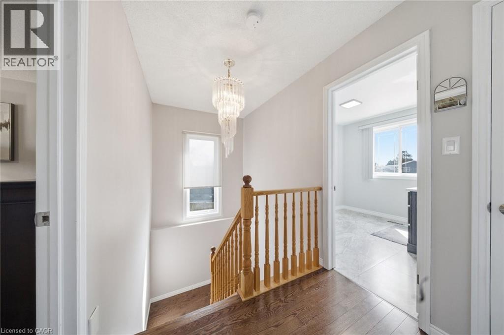 Hallway with wood-finish flooring, a tiered crystal chandelier, and a wood baluster staircase - 200 Morrison Drive, Caledonia, ON - Indoor Photo Showing Other Room