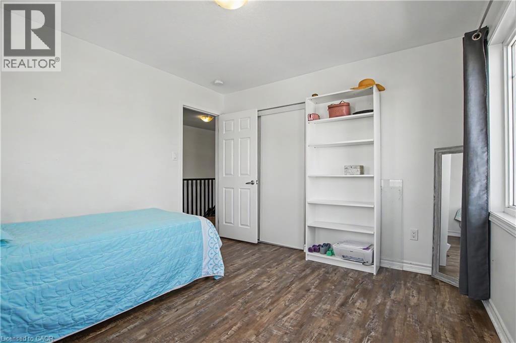 Room featuring wood-finish flooring, a white interior door, a bi-fold closet door, a window with trim, and a ceiling-mounted light fixture - 60 Postmaster Drive, Kitchener, ON - Indoor Photo Showing Bedroom