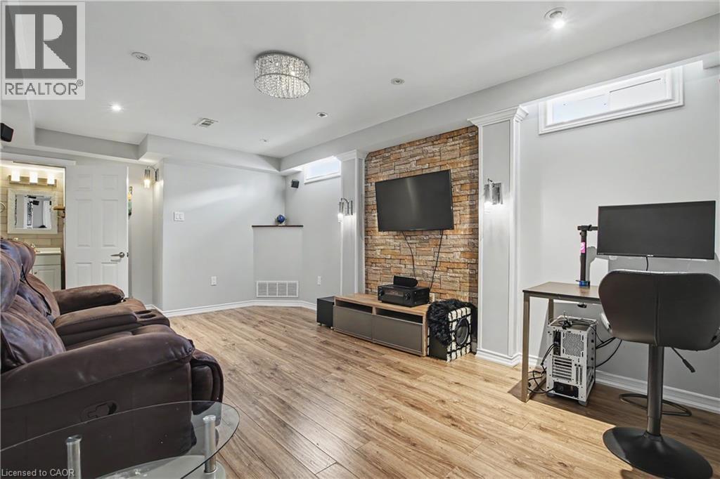 Spacious recreation area featuring wood-finish flooring, a stone accent wall, recessed lighting, and a crystal chandelier - 60 Postmaster Drive, Kitchener, ON - Indoor