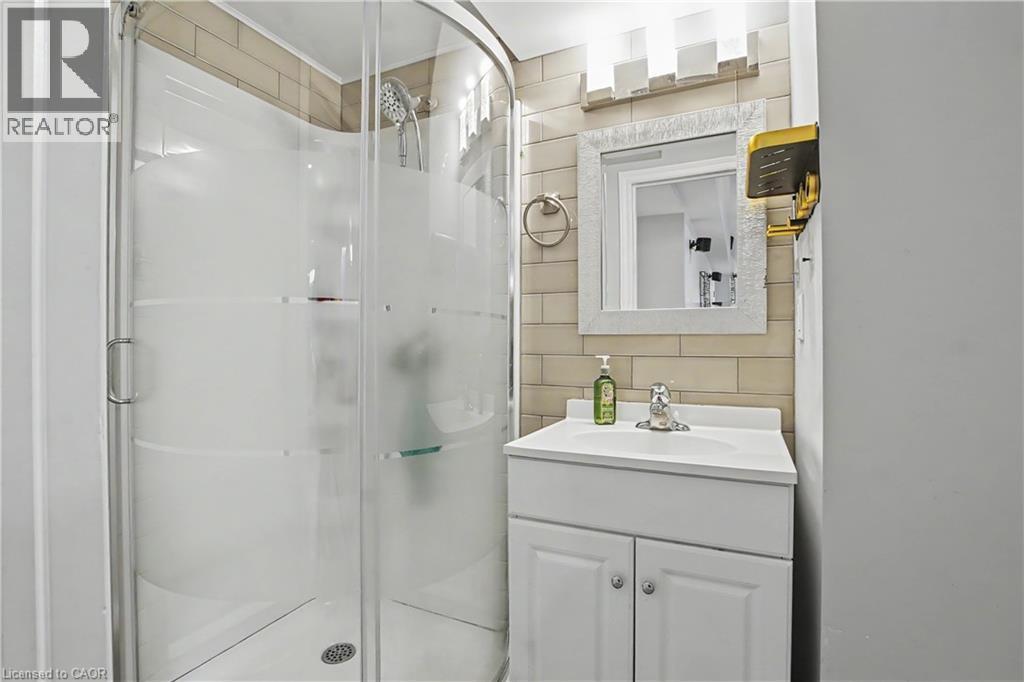 Compact bathroom featuring a curved glass shower enclosure with frosted accents, a white vanity with an integrated sink, a framed mirror, and a wall-mounted light fixture - 60 Postmaster Drive, Kitchener, ON - Indoor Photo Showing Bathroom
