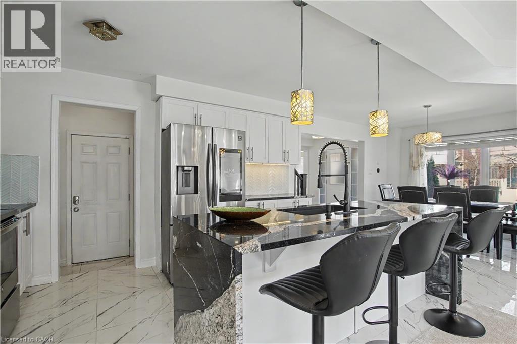Gourmet kitchen featuring a large island with waterfall countertop, stainless steel appliances, white cabinetry, and pendant lighting - 60 Postmaster Drive, Kitchener, ON - Indoor Photo Showing Other Room