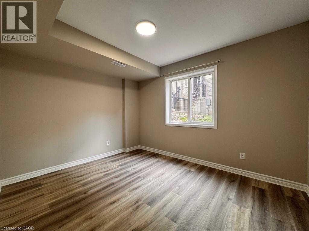 Room featuring wood-finish flooring, neutral wall paint, white baseboards, and a window with white trim - 44 Walnut Street Unit# E01, Kitchener, ON - Indoor Photo Showing Other Room