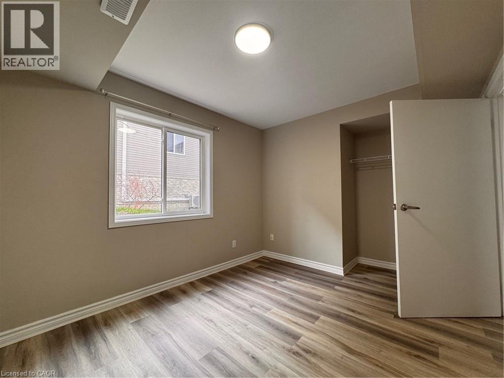 Spacious room featuring wood-finish flooring, neutral-toned walls, a large window, a built-in closet with wire shelving, and a flush-mount ceiling light fixture - 44 Walnut Street Unit# E01, Kitchener, ON - Indoor Photo Showing Other Room