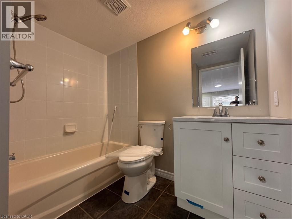 Bathroom featuring a white vanity with integrated sink, a framed mirror, and a tub with white tile surround - 44 Walnut Street Unit# E01, Kitchener, ON - Indoor Photo Showing Bathroom