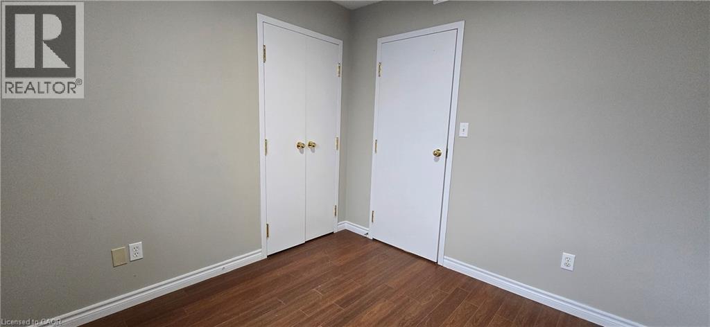 Interior space featuring wood-finish flooring, light-toned walls, white baseboards, and two white doors with brass-toned hardware - 274 E Highland Road E Unit# 10, Kitchener, ON - Indoor Photo Showing Other Room