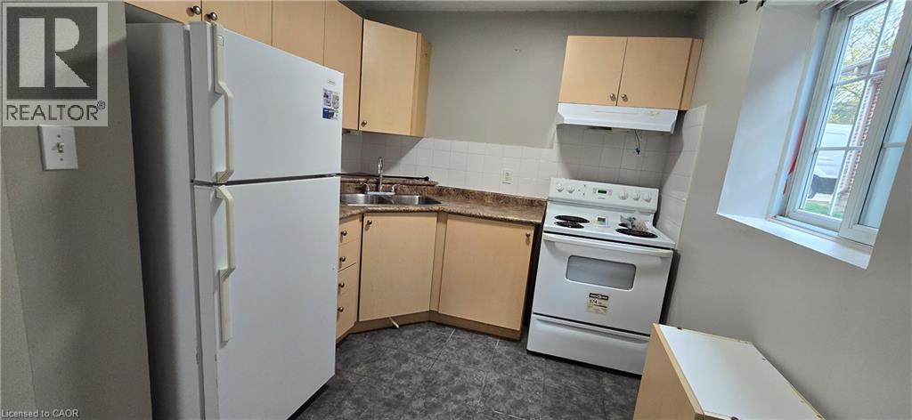 Kitchen featuring light wood-finish cabinetry, white appliances, corner sink, and a window for natural light - 274 E Highland Road E Unit# 10, Kitchener, ON - Indoor Photo Showing Kitchen With Double Sink
