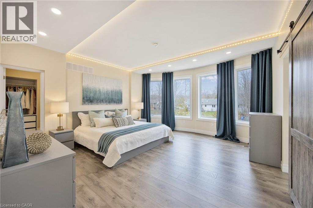 Spacious bedroom featuring wood-finish flooring, a curved wall with multiple windows, recessed ceiling lighting, and a barn door entry - 6 Dorothys Drive, Oro-Medonte, ON - Indoor Photo Showing Bedroom