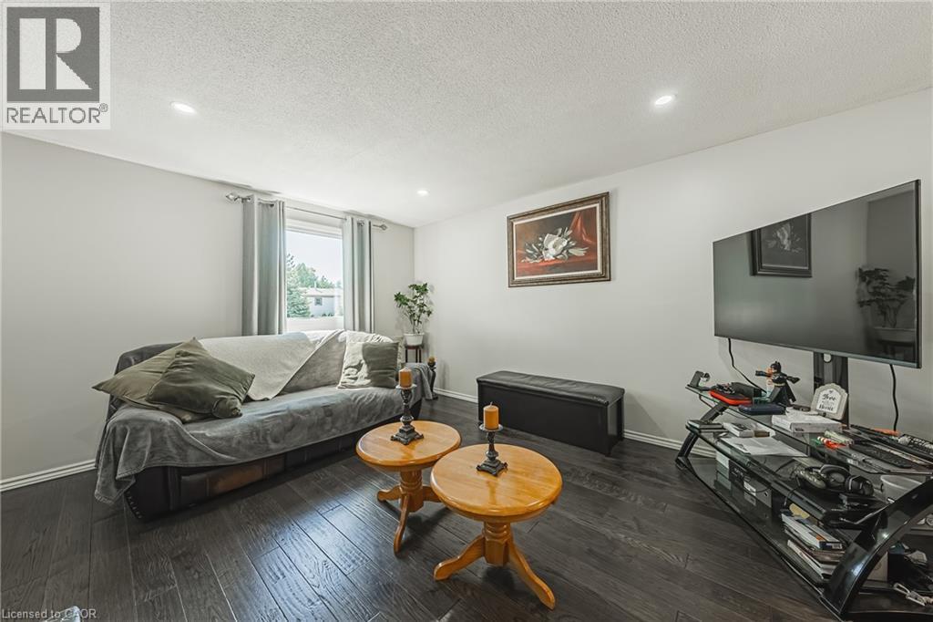 Living area featuring dark wood-finish flooring, recessed ceiling lighting, and a window with blinds - 235 Larch Street, Hamilton, ON - Indoor Photo Showing Living Room