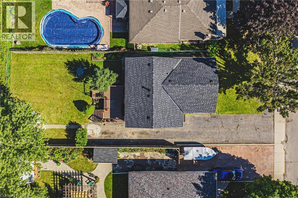 Asphalt shingle roofing, expansive green lawn, wood deck, concrete driveway, and mature trees - 235 Larch Street, Hamilton, ON - Outdoor