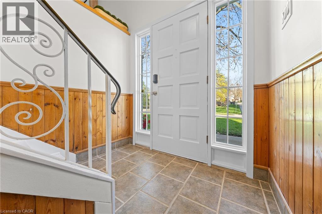 Entryway featuring a paneled front door with sidelight windows, wood-finish wainscoting, decorative wrought iron stair railing, and large format tile flooring - 183 Harvard Road, Waterloo, ON - Indoor Photo Showing Other Room