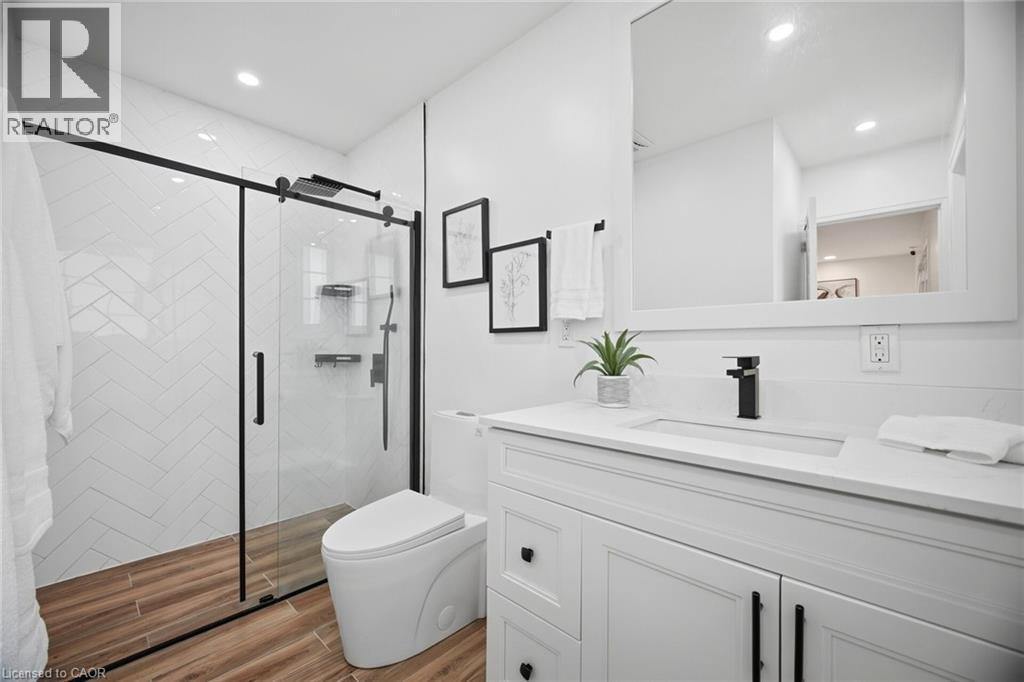 Modern bathroom featuring a glass-enclosed shower with black framing, white subway tile in a herringbone pattern, and wood-finish flooring - 1376 Royal Drive, Burlington, ON - Indoor Photo Showing Bathroom