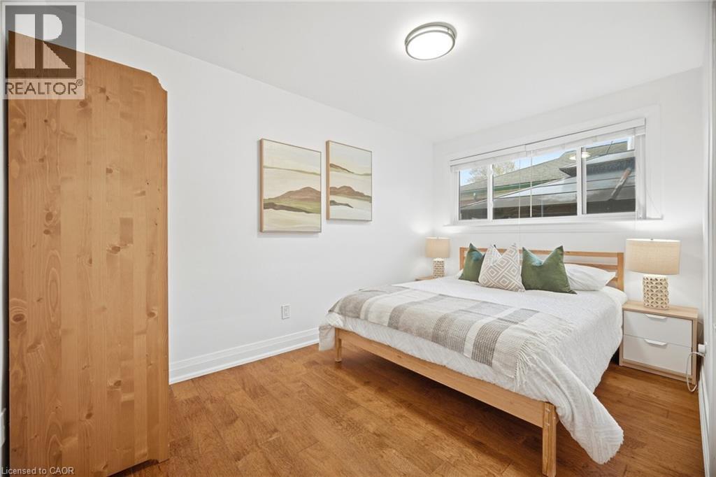 Bedroom featuring wood-finish flooring, a large window with white trim, a flush-mount ceiling light fixture, and a natural wood-panel accent wall - 1376 Royal Drive, Burlington, ON - Indoor Photo Showing Bedroom
