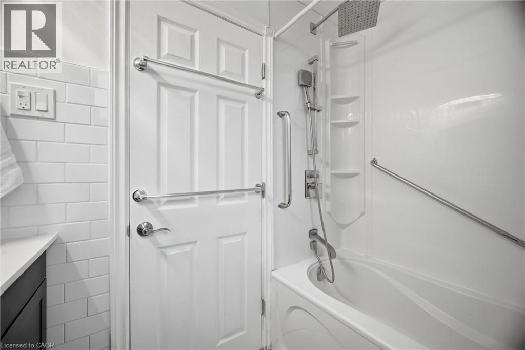 Bathroom featuring a white subway tile wall, a dark vanity with a light countertop, a white paneled door with chrome towel bars, and a white bathtub with a shower system including a rainfall shower he - 1376 Royal Drive, Burlington, ON - Indoor Photo Showing Bathroom
