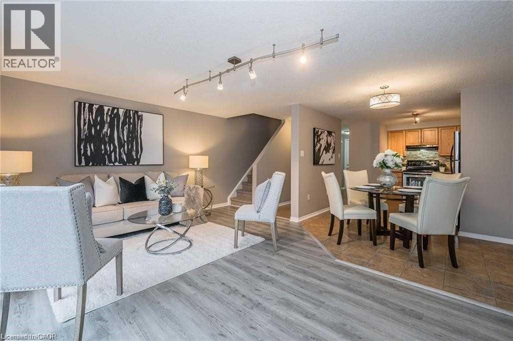 Open-concept living and dining areas featuring wood-finish flooring, track lighting, a staircase with carpeting, and an adjacent kitchen with wood cabinetry - 27 Max Becker Drive, Kitchener, ON - Indoor