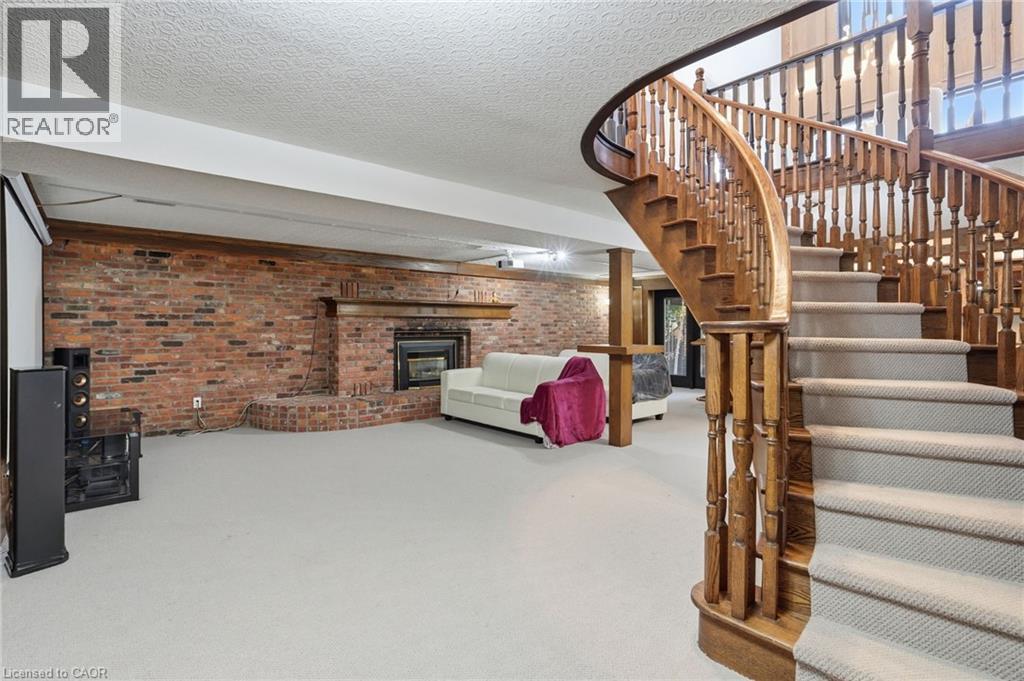 Spacious lower level featuring a grand wooden curved staircase, carpeted flooring, a brick accent wall, and a built-in fireplace - 176 Albion Falls Boulevard, Hamilton, ON - Indoor Photo Showing Other Room
