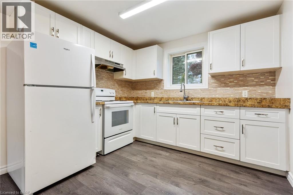 Kitchen featuring white cabinetry, a mosaic tile backsplash, wood-finish flooring, a stainless steel sink, and white appliances - 9 Cherry Street, Simcoe, ON - Indoor Photo Showing Kitchen