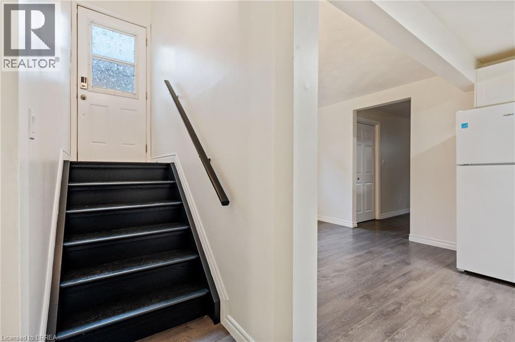 Entryway featuring a white door with frosted glass paneling, a dark-toned staircase with a black handrail, and wood-finish flooring extending into the adjacent space - 9 Cherry Street, Simcoe, ON - Indoor Photo Showing Other Room