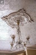 Ornate ceiling medallion with intricate detailing, featuring a multi-arm chandelier with glass shades and crystal accents -