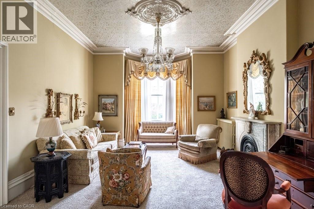 Living area featuring an ornate ceiling medallion, crystal chandelier, decorative ceiling, bay window, and a marble fireplace with a decorative mantel and hearth - 370 Hess Street S, Hamilton, ON - Indoor