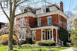 Brick exterior featuring an intricate white cornice, multiple dormer windows, a covered front porch with decorative columns, and an ornate second-story balcony -