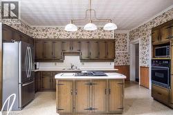 Spacious kitchen featuring extensive dark wood cabinetry, white countertops, and a central island with an integrated cooktop -