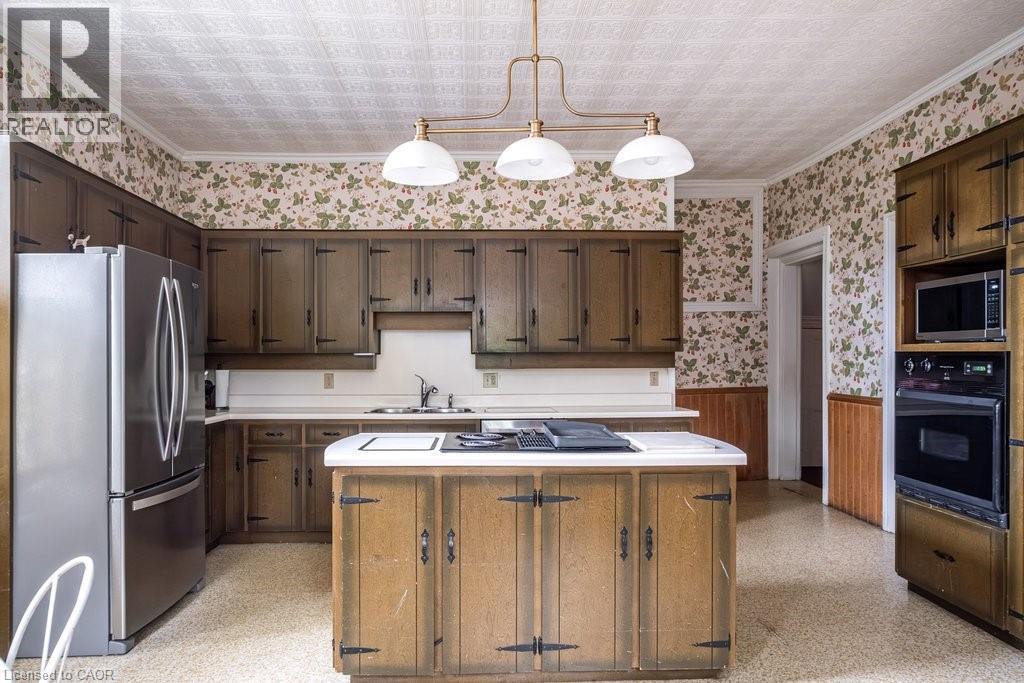Spacious kitchen featuring extensive dark wood cabinetry, white countertops, and a central island with an integrated cooktop - 370 Hess Street S, Hamilton, ON - Indoor Photo Showing Kitchen With Double Sink